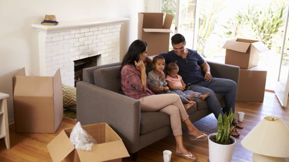family sitting on couch in living room surrounding by half packed boxes